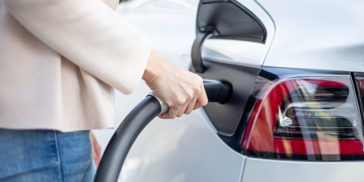 close up of asian woman makes power supply plugged into an electric car being charged