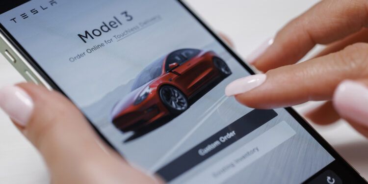 CALIFORNIA, USA - NOVEMBER 14, 2022: Woman using smartphone application. Tesla website, buying a car online. Female touches smart phone close-up. Browsing the different tesla models on their website.