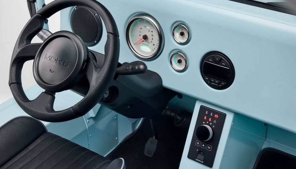un pie de foto del interiorEl interior del MOKE eléctrico Mk2 incorpora un panel de control central, selector de marchas giratorio y conexiones USB-C, además de una toma de 12 V y más espacio para los pies de los pasajeros.